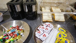 A kitchen counter with two toasters, a glass container with bread, a metal plate with assorted candies, and a plate with butter packets. - Unique Hotel The View (Tongyeong)