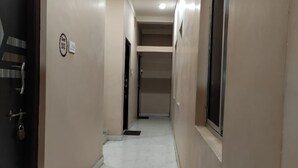 A corridor with beige walls, a dark door on the left, and a window on the right. - Deteex Hotel Baluchar (Mandarmani)