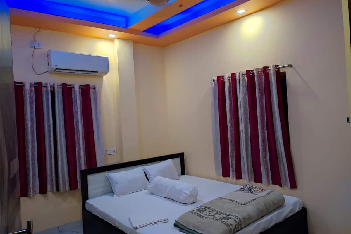 Una habitación de hotel con cama, cortinas, equipo de aire acondicionado e iluminación en el techo.