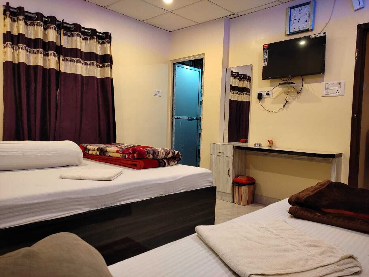 Une chambre d’hôtel avec deux lits, une télévision, une horloge et un petit bureau avec une chaise.