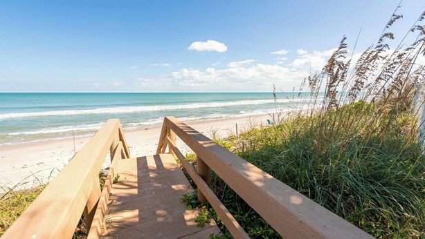A wooden pathway leading to a beach with a clear view of the ocean.