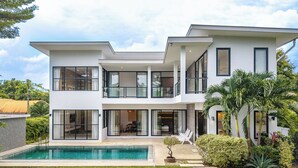 Ein modernes, zweistöckiges Haus mit Swimmingpool, großen Fenstern und einem gepflegten Garten.