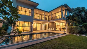 Ein modernes, zweistöckiges Haus mit Swimmingpool, großen Fenstern und einem gepflegten Garten.