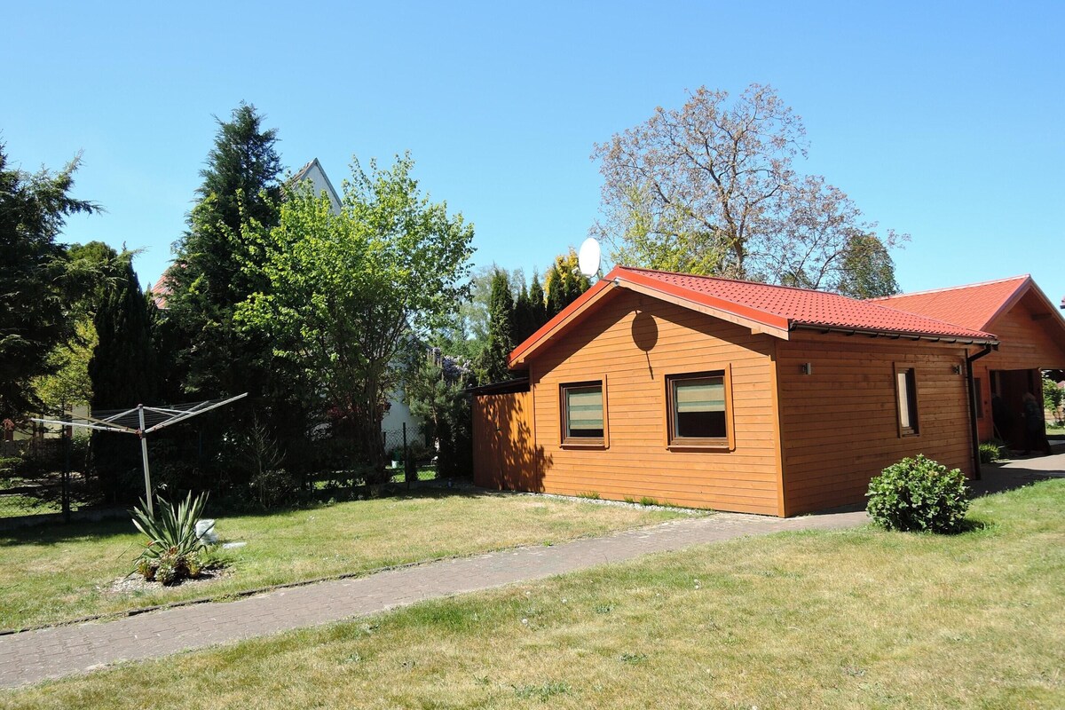 A wooden cabin with a red roof, surrounded by trees and a clear sky.