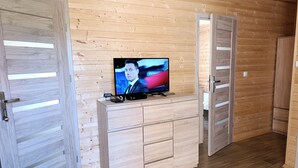 Egy szoba, melynek a falai és a padlója fából van, egy televízió áll egy fa szekrényen, és két fa ajtó található benne.