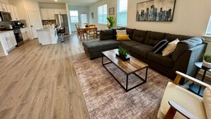 A modern living room with a sofa, coffee table, and a dining area in the background. - Spacious 4BD3BA, Game Room & 2 King Beds & Patio (Austin)