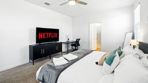A modern hotel room with a bed, a desk, a television displaying 'NETFLIX', and a ceiling fan. - Spacious 4BD3BA, Game Room & 2 King Beds & Patio (Austin)