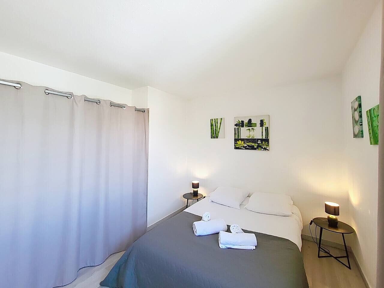 A hotel room with a bed, two bedside tables with lamps, a curtain, and wall art.