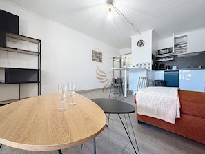 Um espaço de estar moderno com uma mesa de jantar redonda de madeira, um sofá vermelho e uma área de cozinha ao fundo.