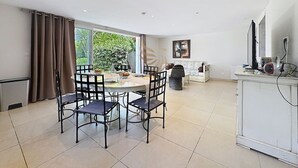 Een moderne woonkamer met een eethoek, grote ramen en uitzicht op groen.