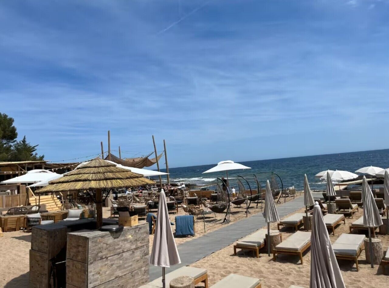 Un complexe hôtelier situé en bord de mer, doté de chaises longues, de parasols et d’une structure à toit de chaume.