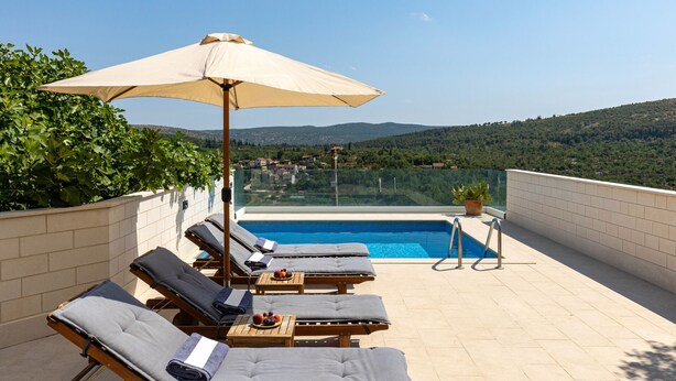 Un espace piscine aménagé sur le toit, avec des chaises longues, une table garnie de fruits et une vue sur le paysage environnant.