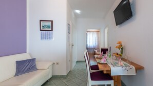 A compact living space with a sofa, a dining table set for two, and a television mounted on the wall. - Apartman Lucija 4 by Villas Guide (Crikvenica)