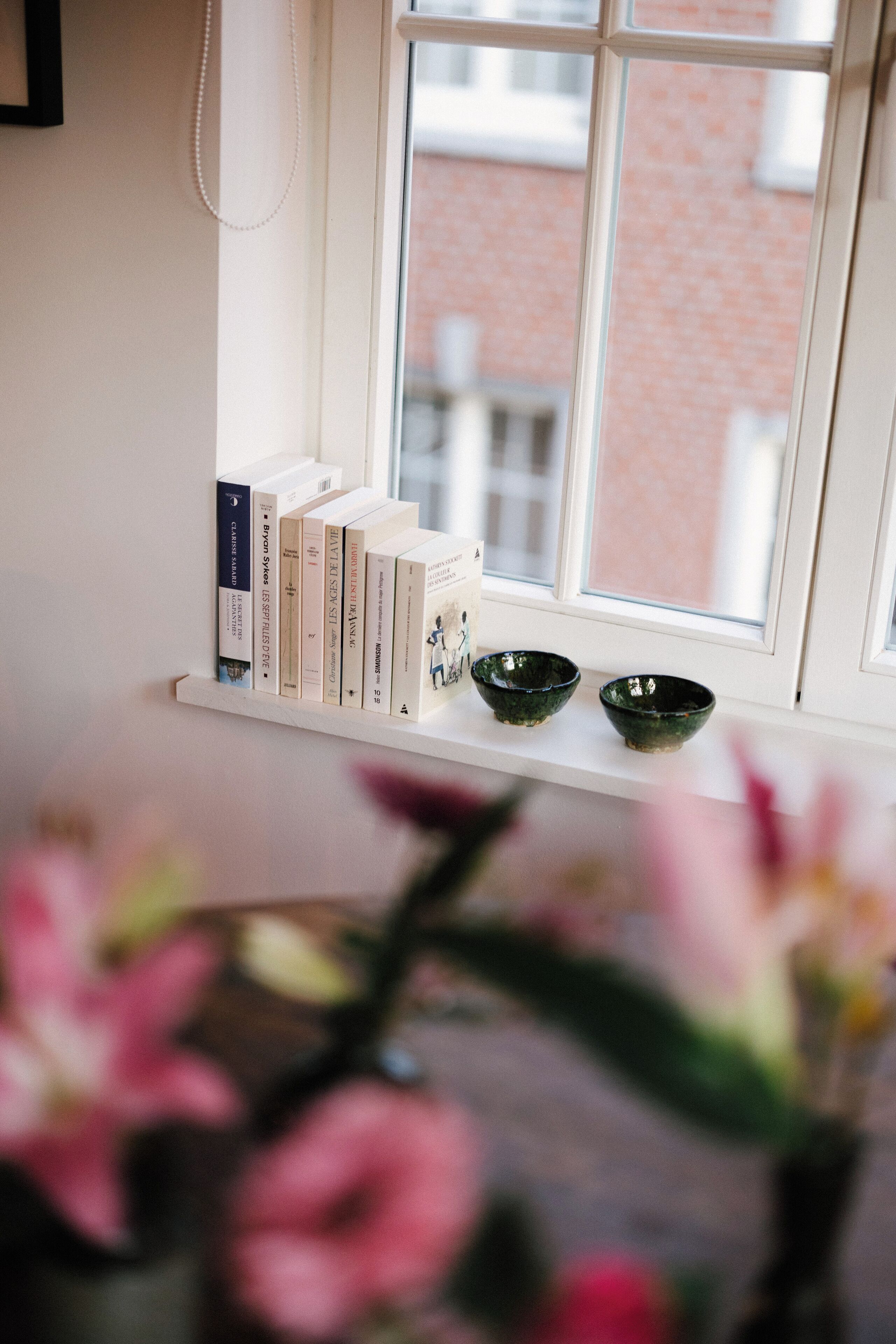 Una ventana con un estante blanco que sostiene libros y dos cuencos verdes.