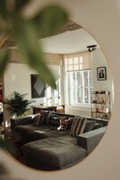 A cozy living room with a sectional sofa, a coffee table, a bookshelf, and a large window providing natural light.