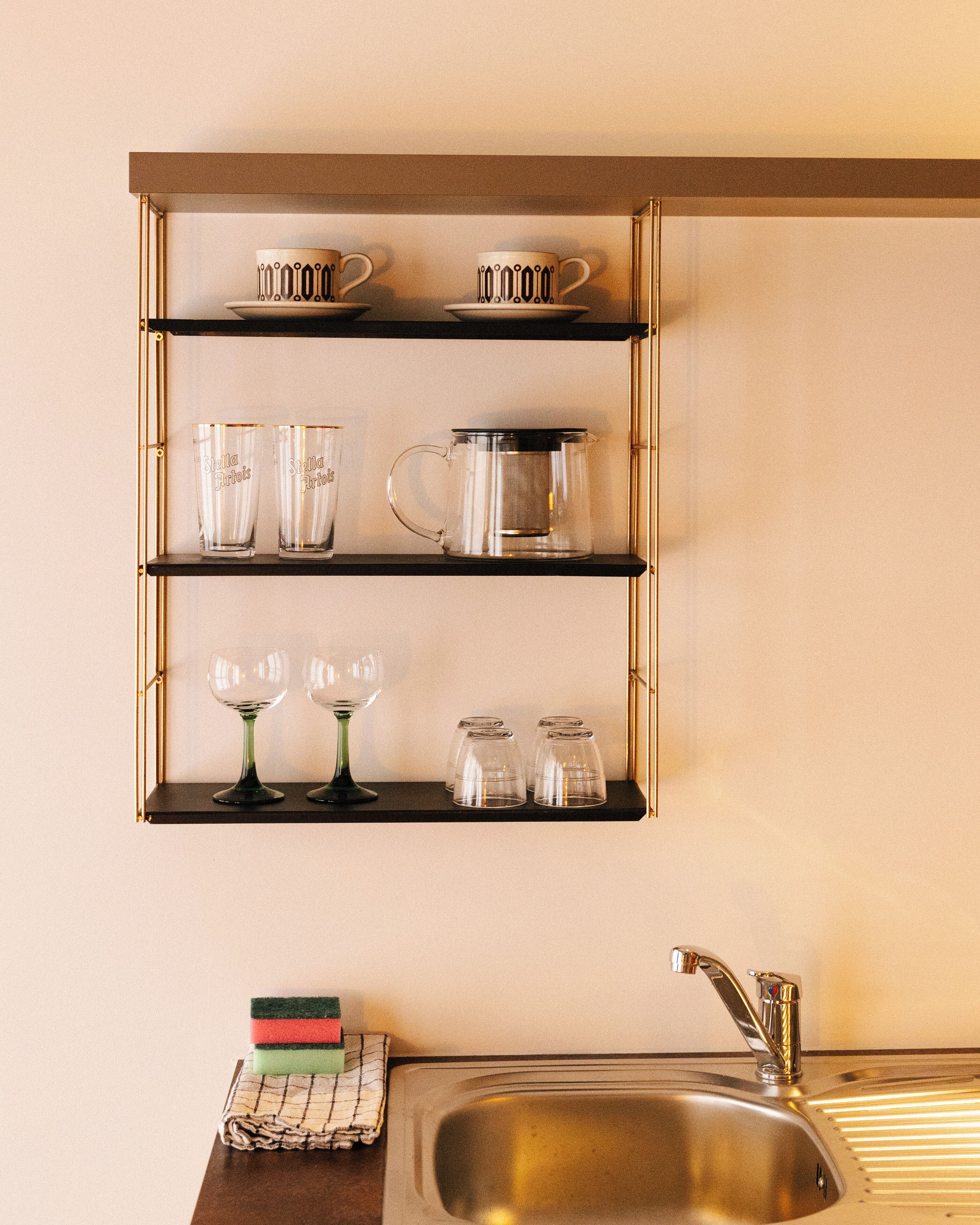A kitchen with a stainless steel sink, a coffee maker, and glassware on shelves.