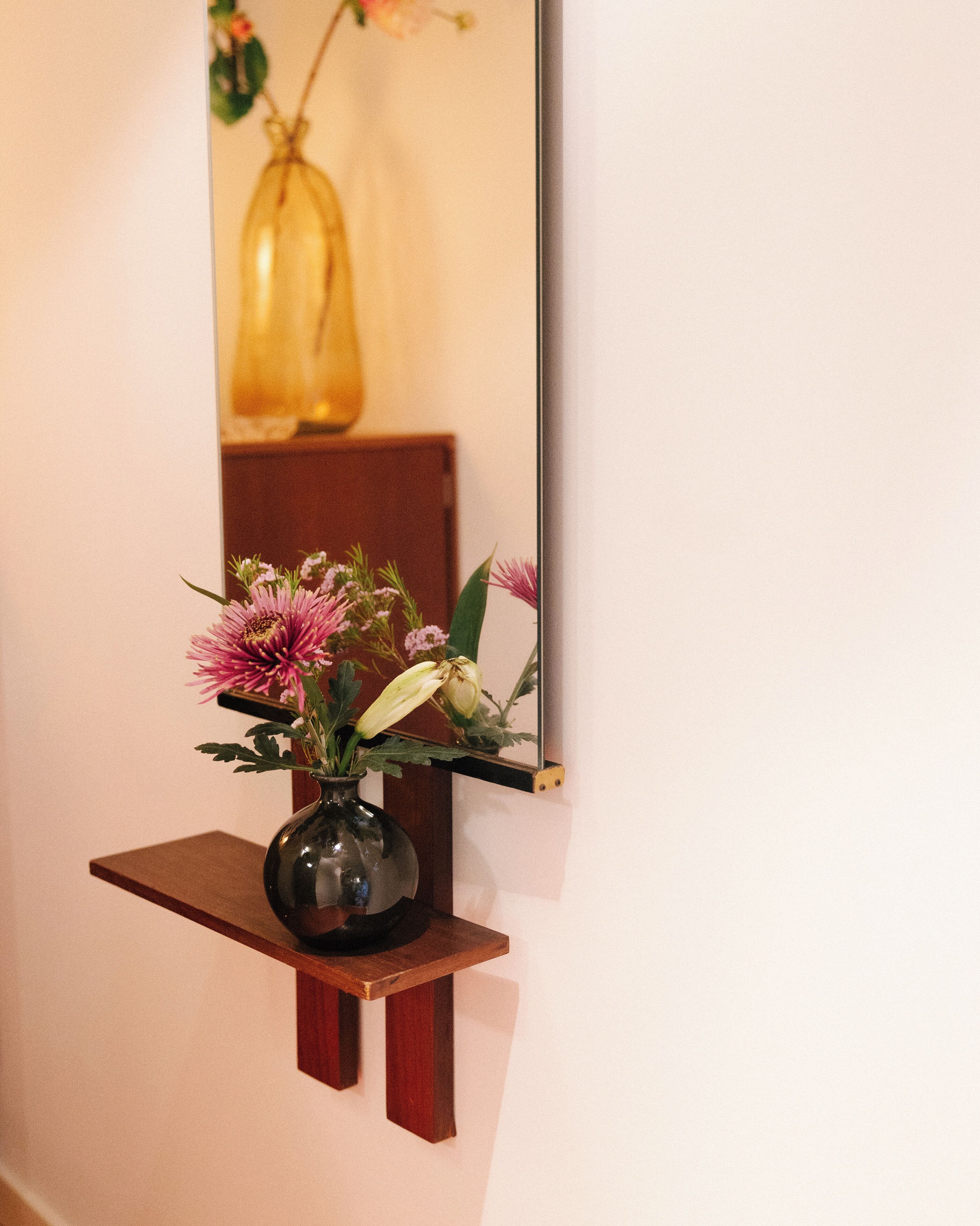 Um vaso com flores sobre uma prateleira de madeira em frente a uma parede.