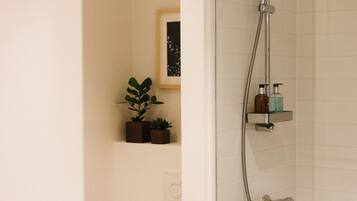 Une salle de bain moderne avec une douche à parois de verre, un miroir, une étagère contenant des articles de toilette et une petite plante.