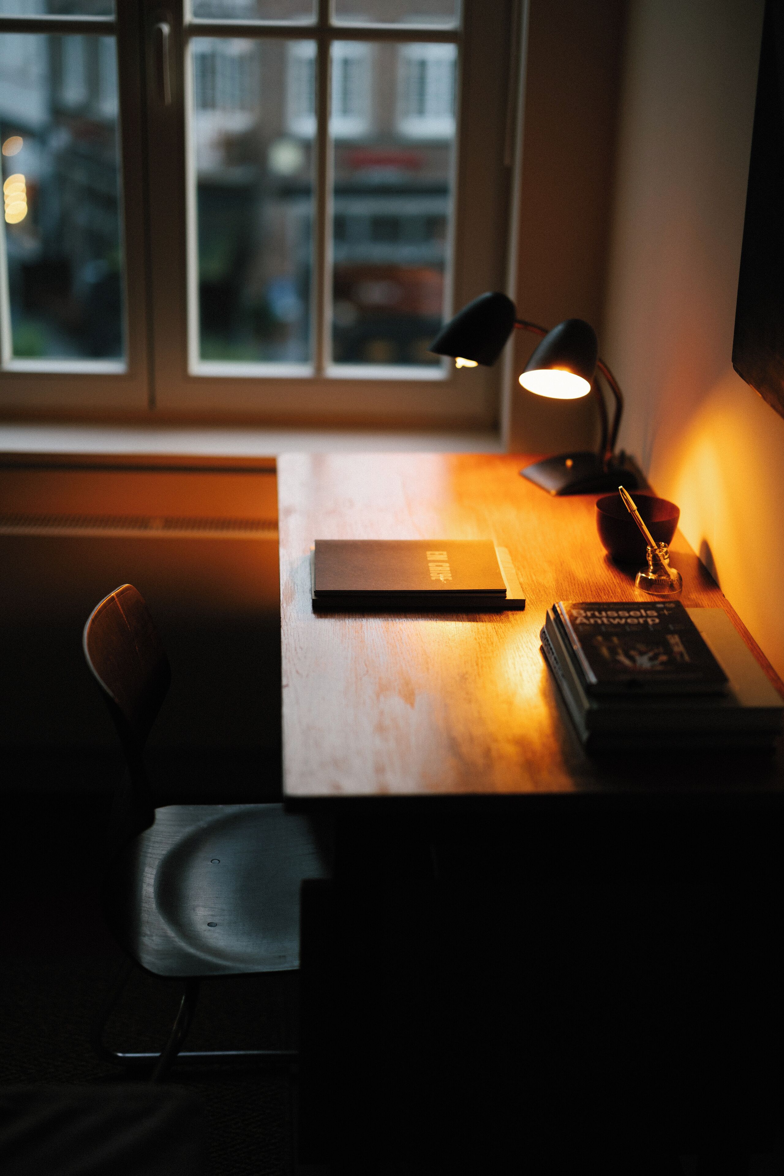 A dimly lit desk with a laptop, a book, and a lamp.
