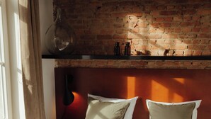 Een slaapkamer met een bakstenen muur, een bed met witte beddengoed en een plank boven het bed.