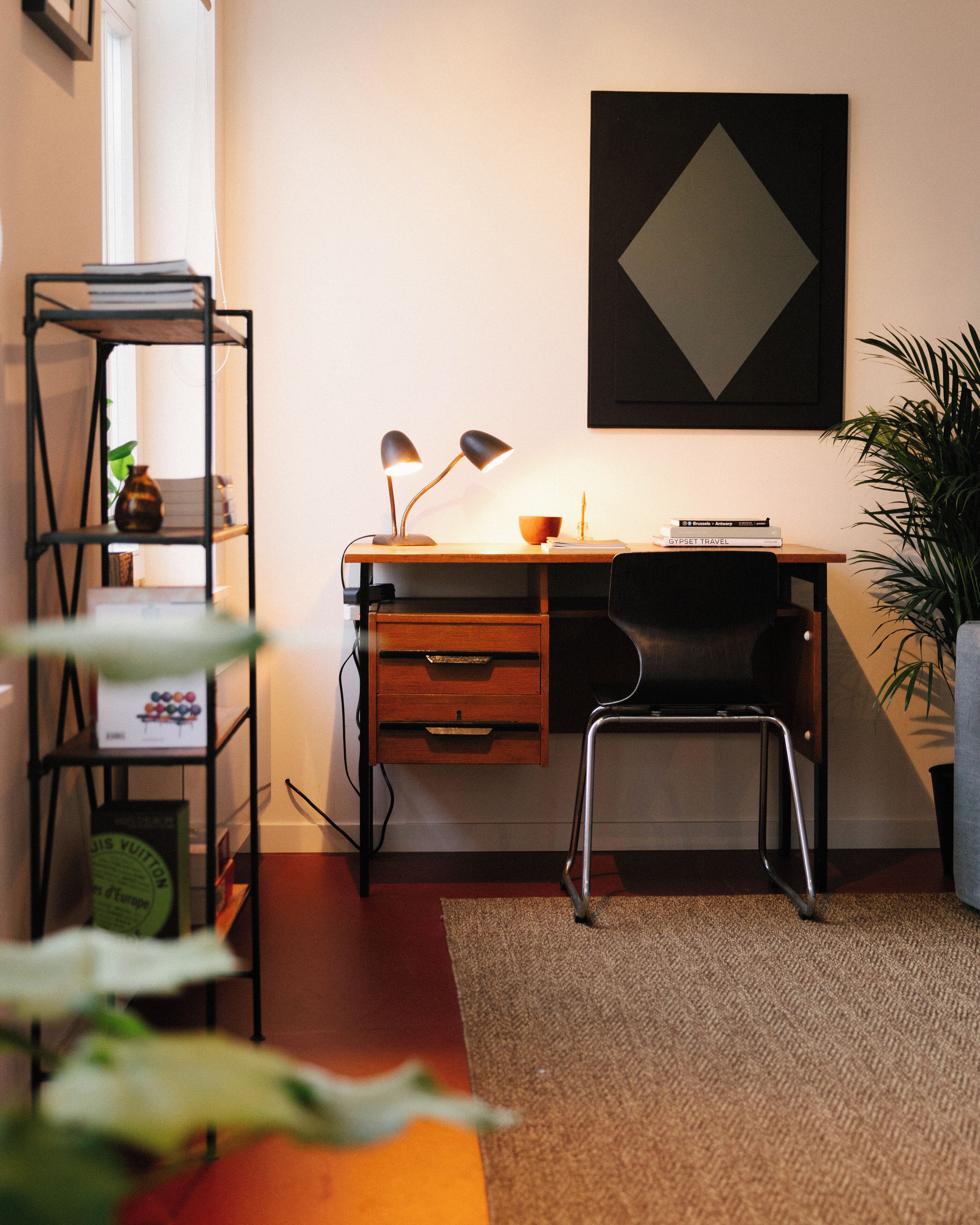A modern office space with a desk, chair, shelves, and a potted plant.