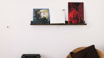Una habitación con dos estantes empotrados que exhiben obras de arte enmarcadas, una maleta negra y un sillón con cojín.