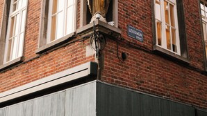 Een gebouw van baksteen met een standbeeld op de hoek, een bord waarop “LEEUVEN STREET” staat en een raam met een witte omlijsting.