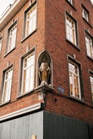 A brick building with a statue on the corner, a sign reading "LEEUVEN STREET," and a window with a white frame.