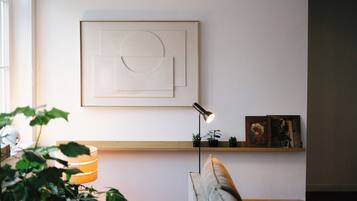 A minimalist living room with a wall-mounted abstract artwork, a floor lamp, a bookshelf with books and plants, and a couch.