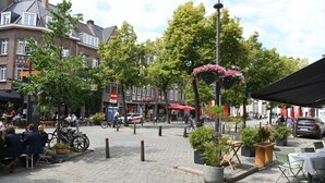 Een geplaveid plein met terrasjes, plantenbakken en fietsen.