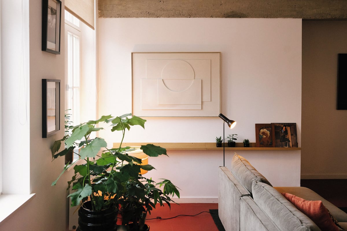 A living room with a grey sofa, a black floor lamp, a large potted plant, and a framed abstract artwork on the wall.