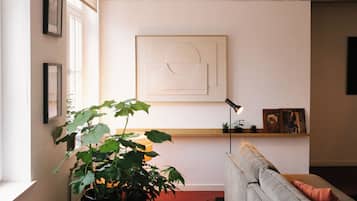 En stue med en grå sofa, en gulvlampe i sort, en stor plantepotte og et abstrakt billede i ramme på væggen.