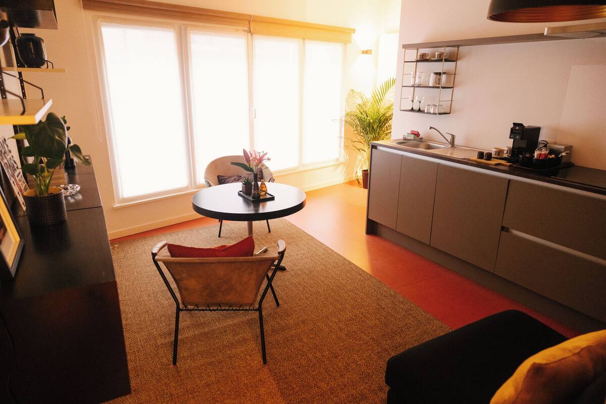 A compact kitchen with a dining area, a coffee machine, and a potted plant.