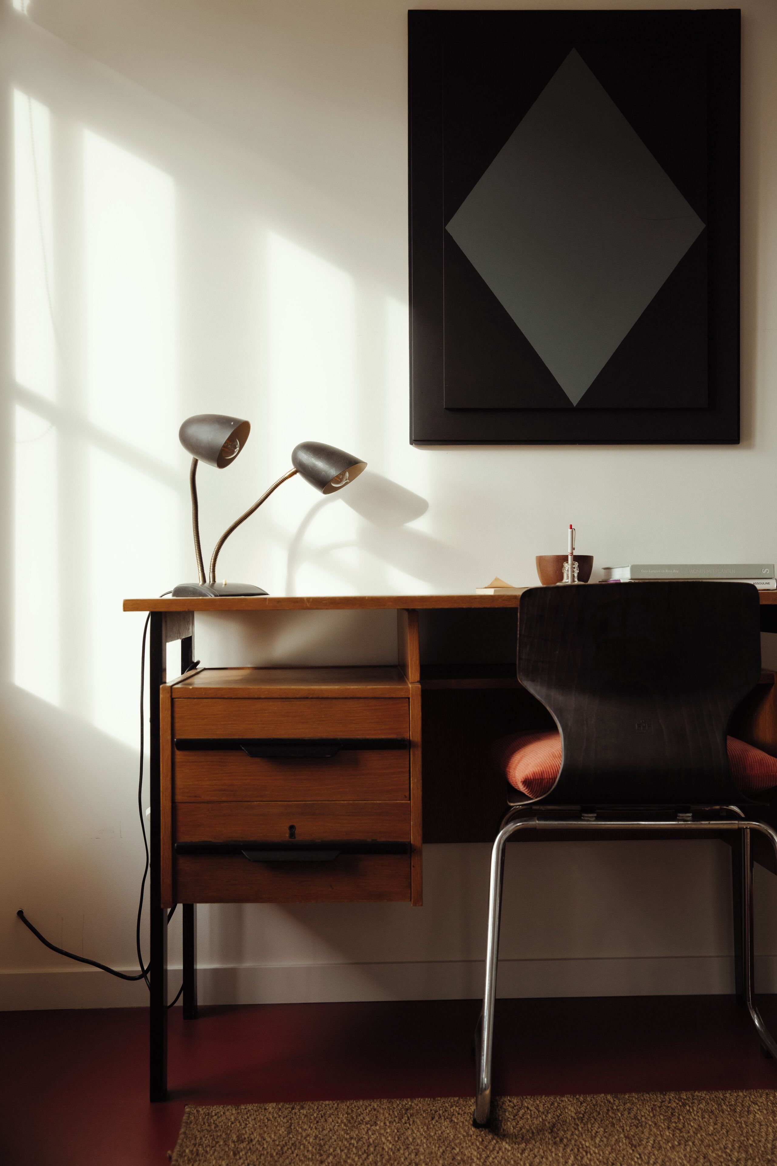 Un escritorio moderno con una lámpara, una silla y una obra de arte enmarcada en la pared.