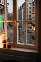 A view through a window with a grid pattern, overlooking a street with buildings and a few pedestrians.