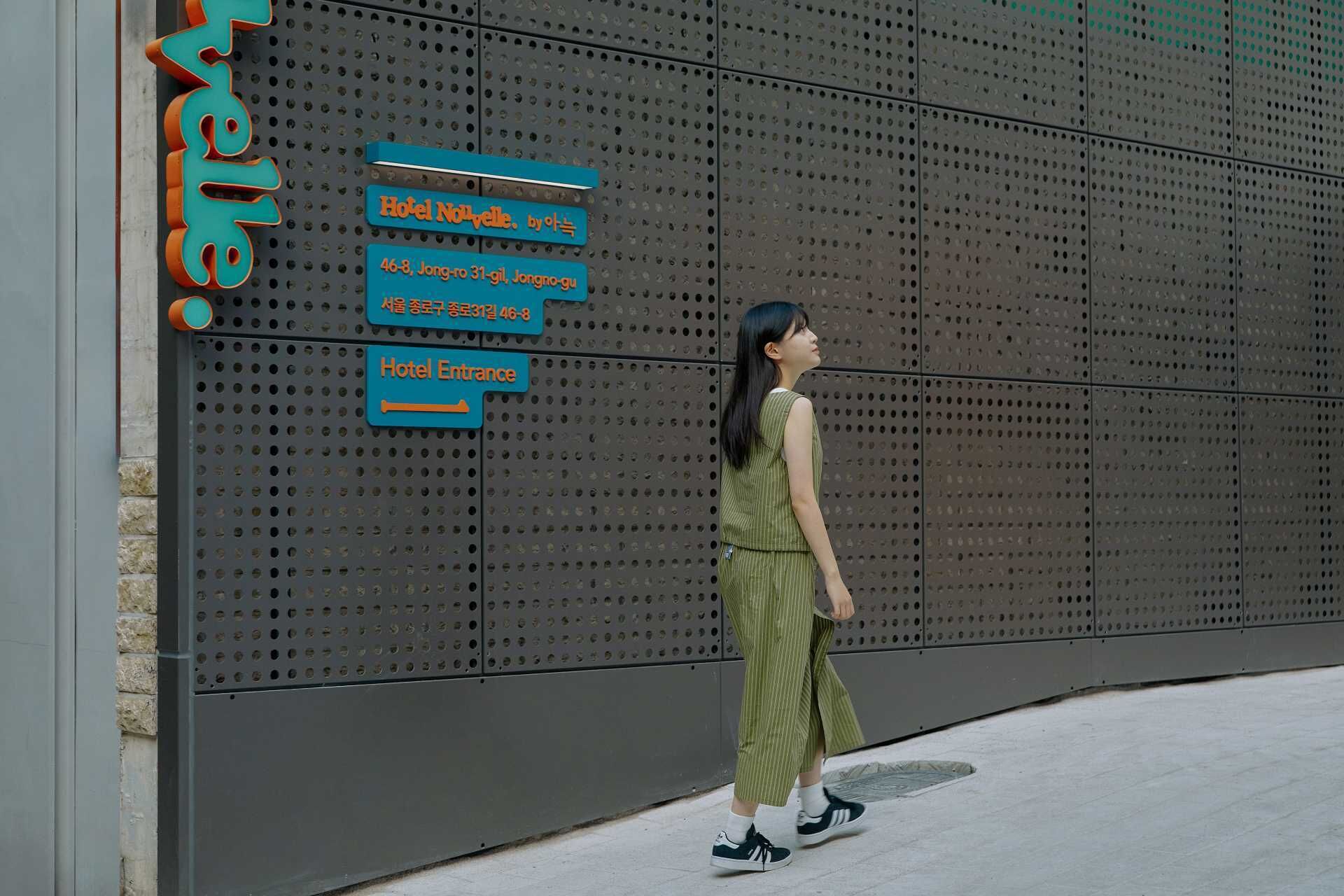 A woman walking past a hotel entrance sign with directions to the hotel and its address.