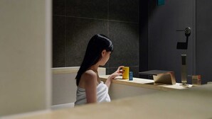 A person in a bathroom with a towel, a yellow cup, and a mirror.