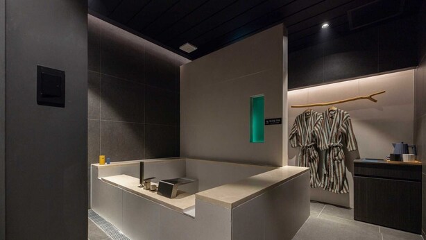 A modern bathroom with a large bathtub, a towel rack with robes, and a small sink area.