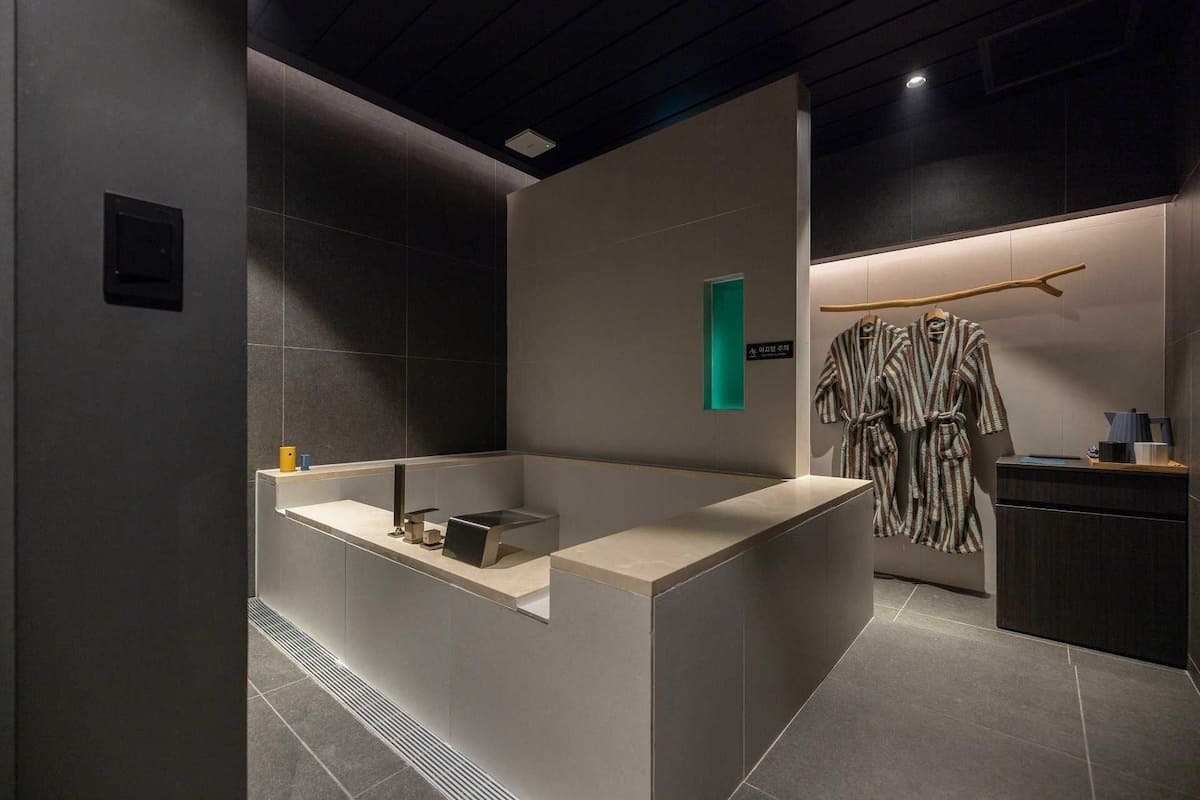 Un baño moderno con una bañera grande, un perchero con batas y una pequeña zona de lavamanos.