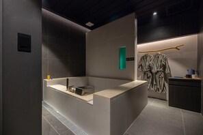 A modern bathroom with a large bathtub, a towel rack with robes, and a small sink area. - Nouvelle Hotel and Spa by Anook Seoul Jongro (Seoul)