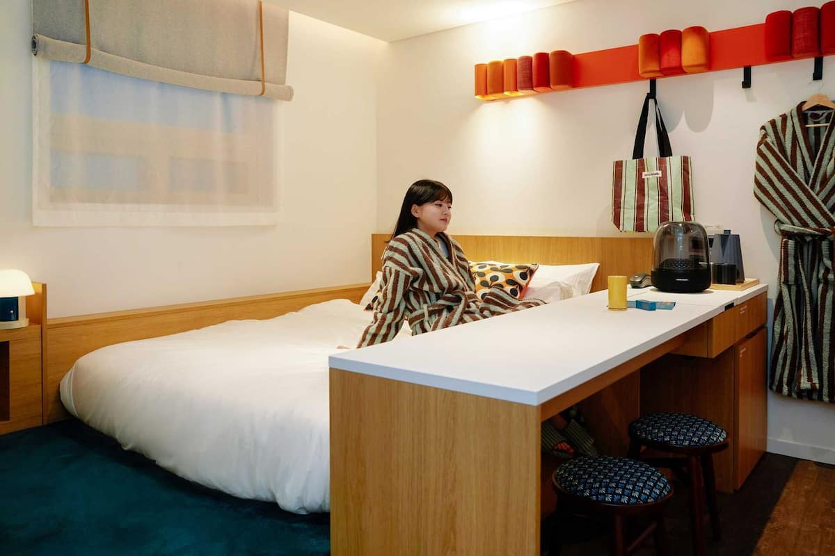Una habitación de hotel compacta con una cama, un escritorio pequeño y una zona de estar con taburetes.