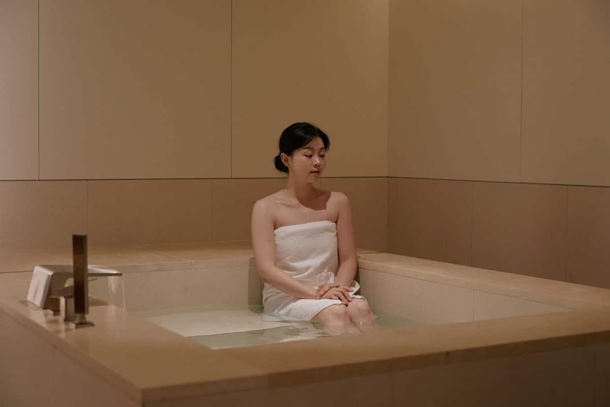 Une personne assise dans une baignoire, dans une pièce dont les murs sont unis et qui contient un banc.