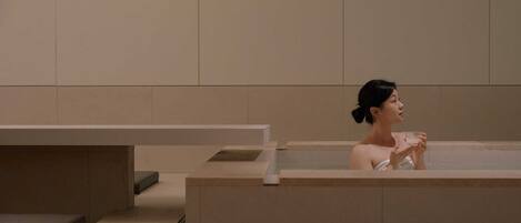 A person in a bathtub in a modern, minimalist bathroom with clean lines and neutral colors.