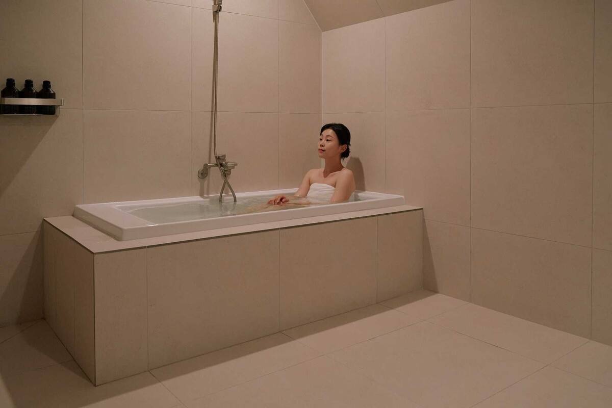 Une salle de bain moderne avec une grande baignoire, une douche et une étagère où sont rangés les produits de toilette.