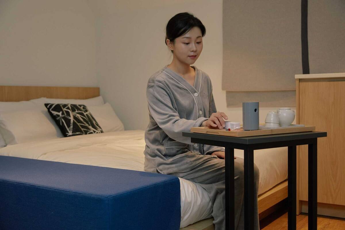 Une personne est assise sur un lit dans une chambre d’hôtel et utilise un ordinateur portable sur une petite table.