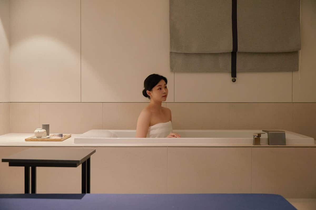Une salle de spa avec une baignoire, une petite table avec une tasse et un récipient, et une serviette accrochée au mur.