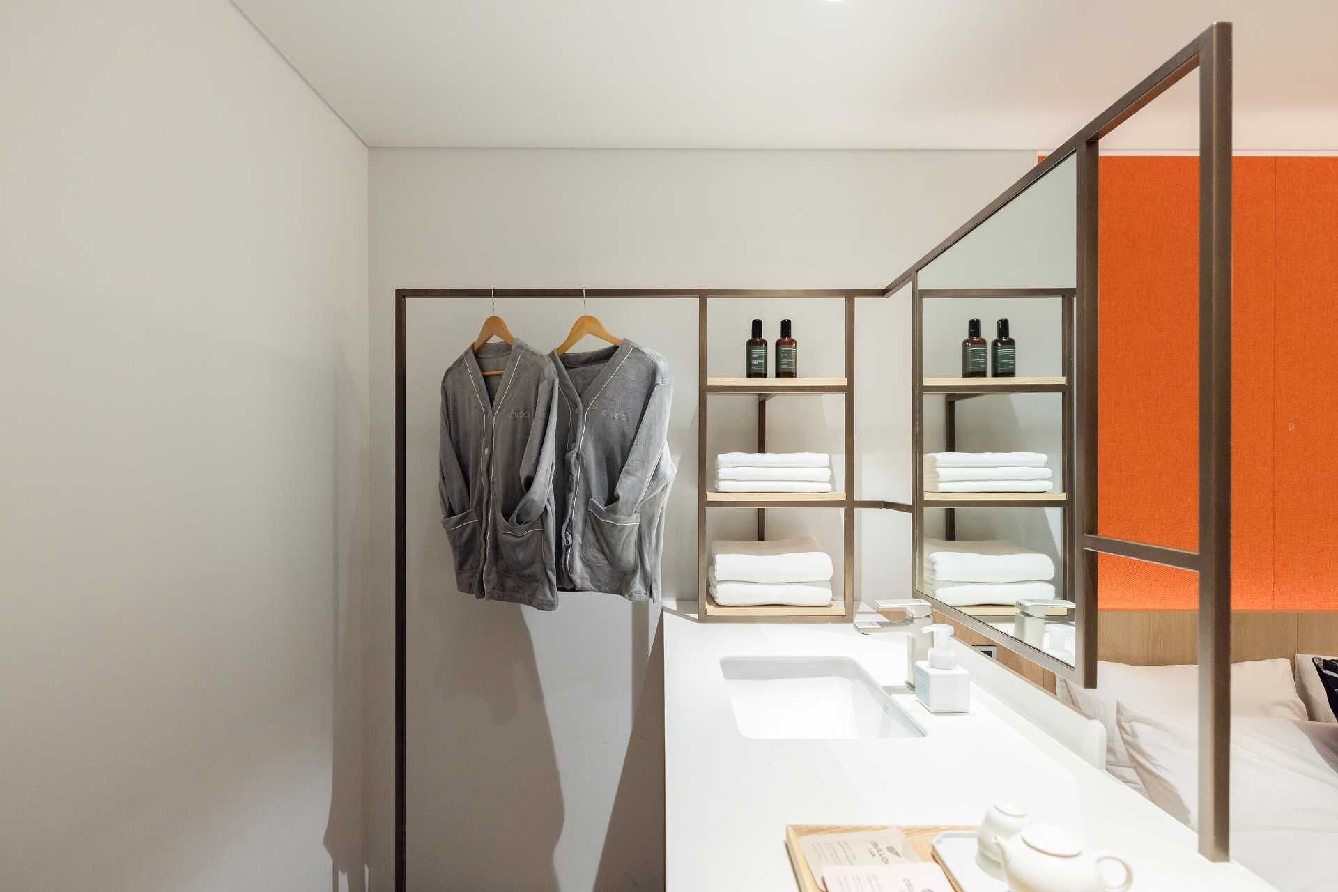 A modern bathroom with a large mirror, a white sink, and shelves with toiletries.