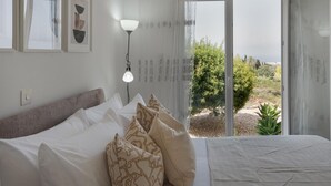 Un dormitorio con cama, almohadas, una lámpara de noche y vistas al exterior.