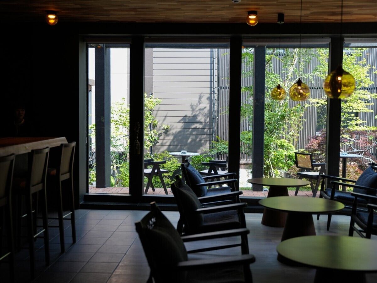An indoor seating area with tables and chairs, large windows, and hanging pendant lights.
