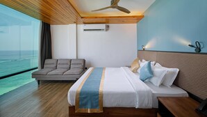 A hotel room with a bed, a sofa, a ceiling fan, an air conditioning unit, and a view of the ocean.